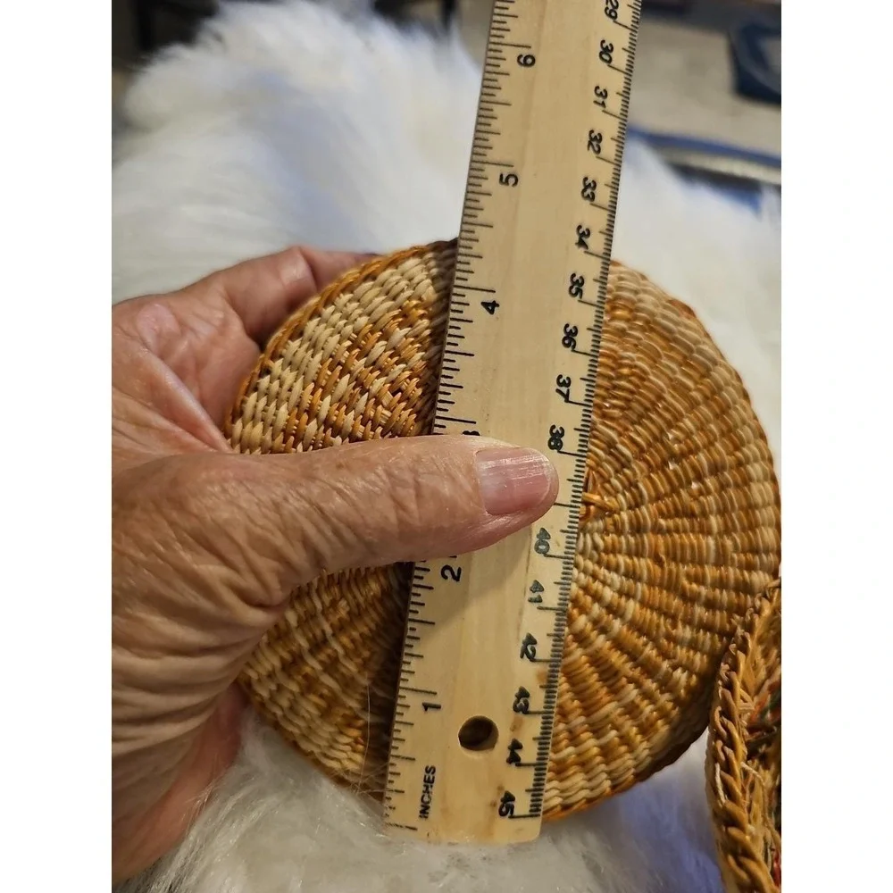 The image displays a‎ small, round, hand-woven basket with a lid, typically made